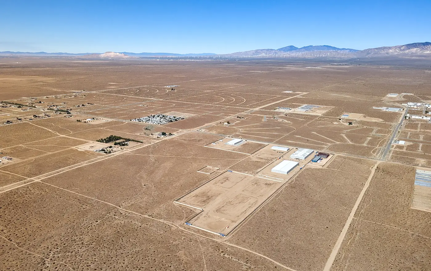 Aerial photograph of the edge of California City's built area: a few industrial buildings and yards along a road, and around them a wide grid of graded streets and cul-de-sacs laid out across bare desert with nothing built along them.